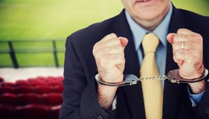 Closeup of businessman with handcuffed hands against red bleachers looking down on football pitch